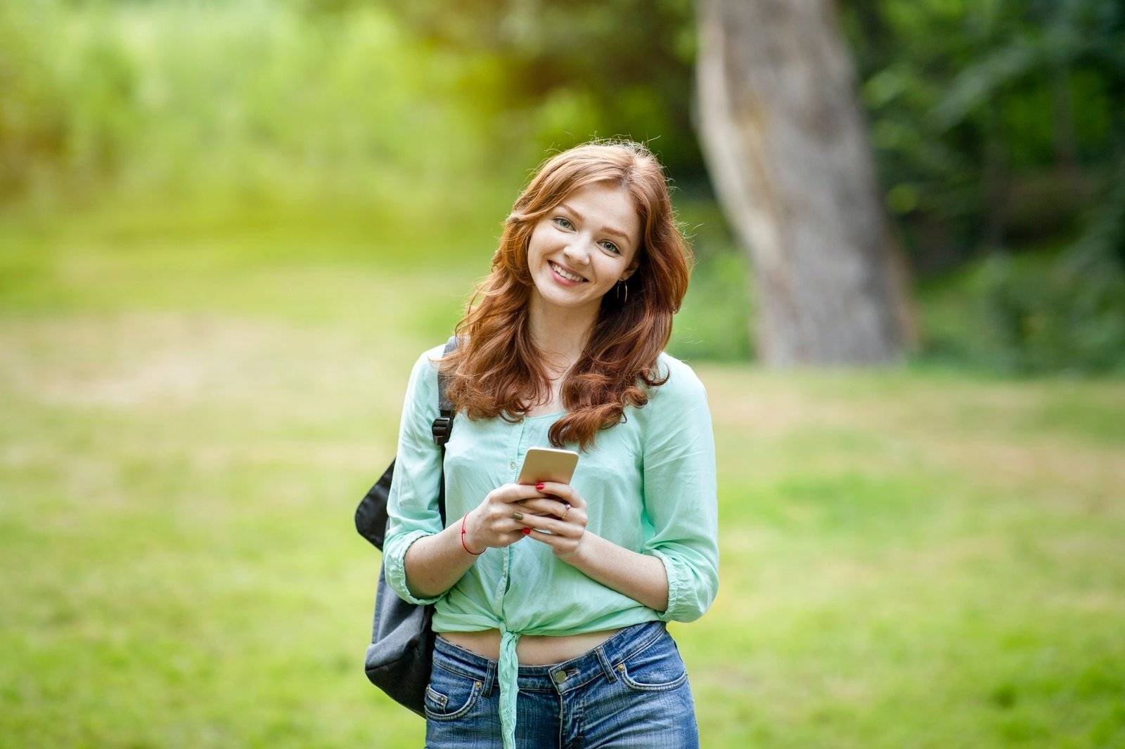 portrait of cute redhead teen girl with backpack and smartphone
